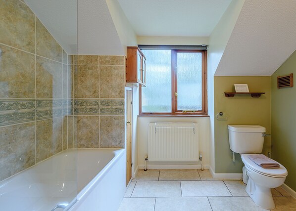 A bathroom with a bathtub, toilet, and window.