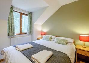 Ein Schlafzimmer mit einem Bett, zwei Nachttischlampen, einem Fenster mit Vorhängen und einer Heizung.