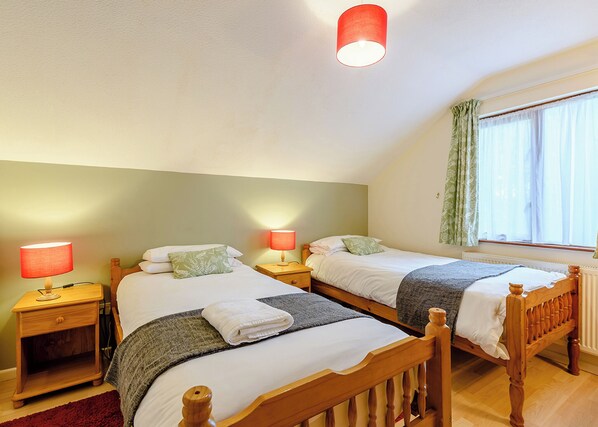 A bedroom with two wooden beds, nightstands with lamps, a window with curtains, and a radiator. - 2 bedroom accommodation in Webbery, Bideford (Webbery, Bideford)