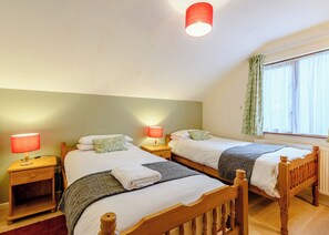 A bedroom with two wooden beds, nightstands with lamps, a window with curtains, and a radiator. - 2 bedroom accommodation in Webbery, Bideford (Webbery, Bideford)