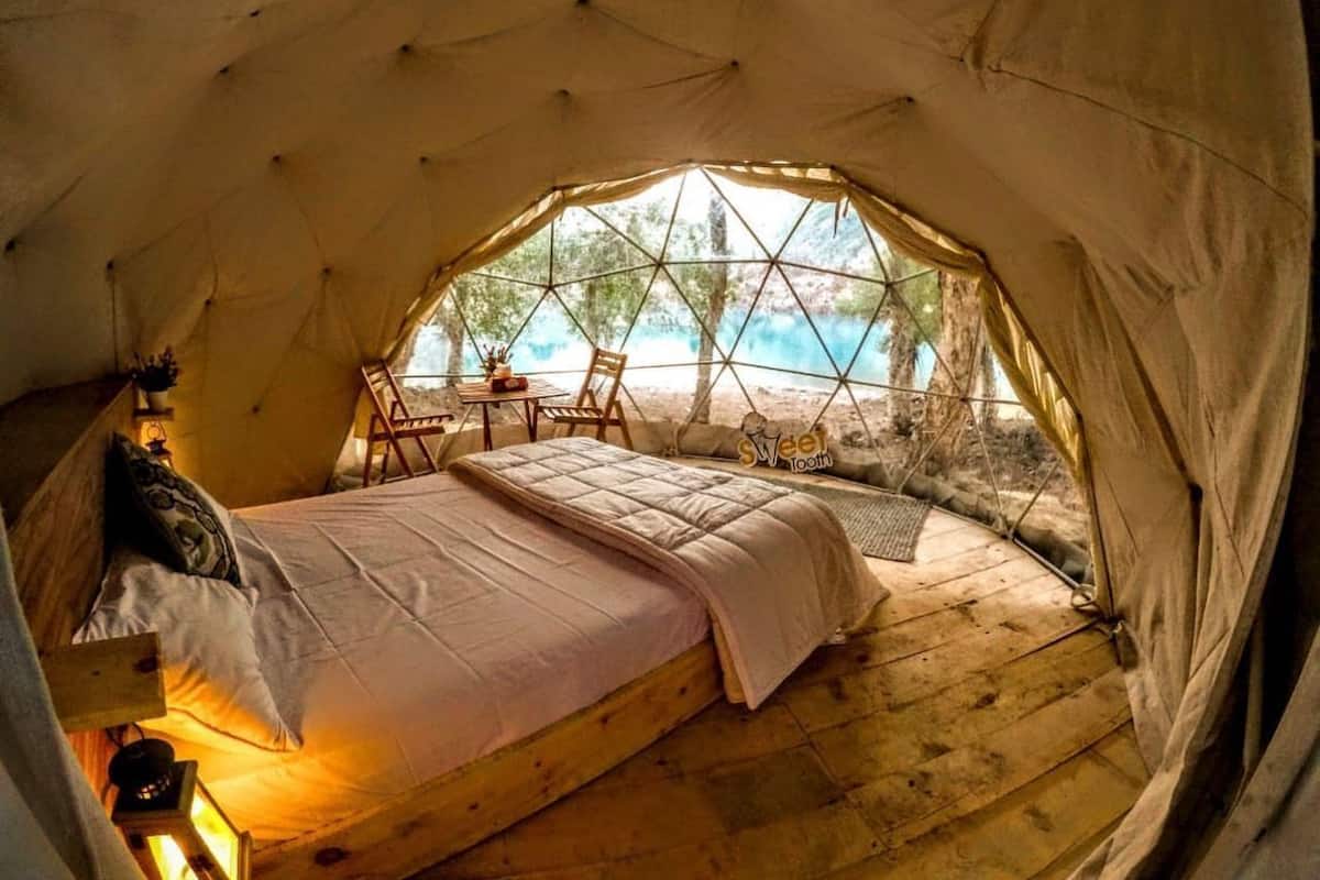 A cozy tent with a bed, a small table, and chairs, overlooking a scenic landscape.