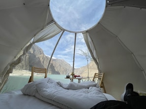 A tent with a bed, a table with a chair, and a view of mountains and water. - Orangeloft Attabad Lake Hunza (Hunza)