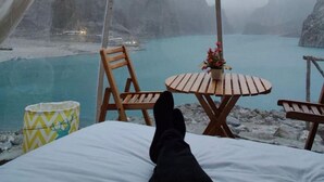 Uma tenda com uma mesa redonda e cadeiras voltadas para uma paisagem montanhosa e um corpo d'água.