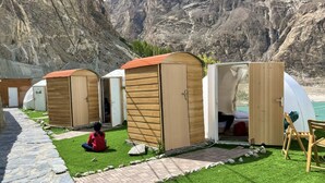 Uma fileira de cabanas de madeira com um caminho de pedra que as leva até elas, ao fundo montanhas.