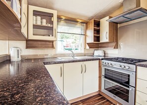 A compact kitchen with a granite countertop, stainless steel appliances, and wooden cabinetry. - 12ft-wide caravan with one double with en suite W. (Tenbury Wells)