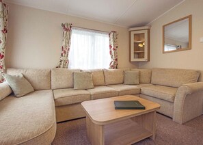 A living room with a beige sectional sofa, a wooden coffee table, and a mirror on the wall.