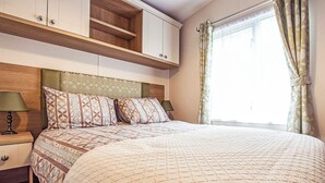 Un dormitori amb llit, nits, un capçal de fusta, una finestra amb cortines i armaris de paret.