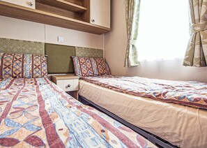 A bedroom with two beds, a nightstand, a wardrobe, and a window with curtains.