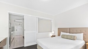 A hotel room with a bed, a desk, a chair, a nightstand, and a window. - One Bedroom in the Heart of  Kangaroo Point with Pool & Parking (Kangaroo Point)