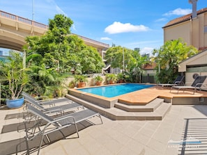 A swimming pool with lounge chairs, surrounded by potted plants and trees.