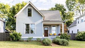 A two-story house with a front porch, a small garden, and a wooden fence. - Cheerful House near Coffee, Food + Fenced-in Yard (Nashville)