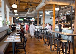 A restaurant with high tables and stools, a bar area, and a television screen in the background.