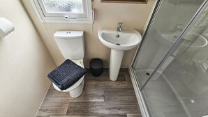 Ett litet badrum med toalett, handfat och en duschkabin med glasväggar.