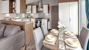 Une cuisine moderne et fonctionnelle, équipée d’un four à micro-ondes, d’une cuisinière et d’un four. Un coin repas est aménagé avec une table pour quatre personnes, comprenant assiettes, verres et couverts.