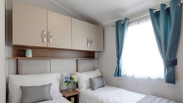 A bedroom with two beds, a wooden headboard, a nightstand with a vase, and a window with curtains.