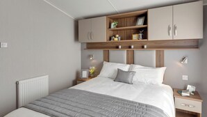 A modern bedroom with a bed, a nightstand, a wooden headboard, and built-in storage cabinets.
