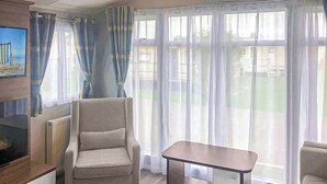 A room with a large window, a chair, a small table, and a TV on a stand.