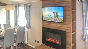 A living room with a fireplace, a flat-screen TV mounted above it, and a dining area with chairs and a table.