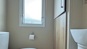 A bathroom with a toilet, a window, and a towel dispenser.