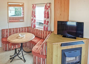 Un coin salon avec des sièges disposés en cercle autour d’une table ronde, un téléviseur posé sur un meuble en bois et une fenêtre avec des rideaux.
