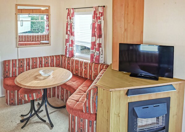 Eine Sitzecke mit rundem Tisch, einem Fernseher auf einem Holzständer und einem Fenster mit Vorhängen.