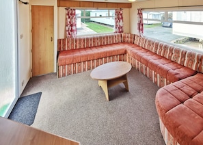 Un intérieur chaleureux avec un canapé d’angle, une table basse ronde et une vue sur l’extérieur.