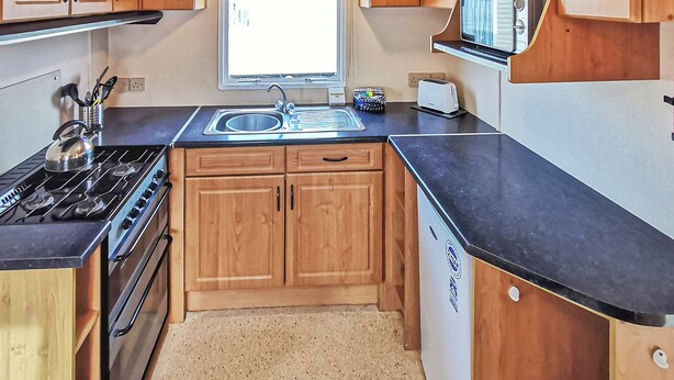 A compact kitchen with wooden cabinets, a gas stove, a sink, and a microwave. - Comfortable caravan with one double and two twin. (Cross Inn, Nr New Quay)