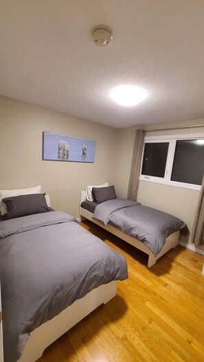 A room with two beds, a ceiling light, a window with curtains, and a picture on the wall. -  YK Aurora B&B  (Yellowknife)