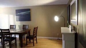 A dining area with a table and chairs, a painting on the wall, and a lamp. -  YK Aurora B&B  (Yellowknife)
