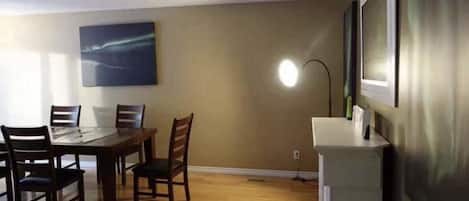 A dining area with a table and chairs, a painting on the wall, and a lamp.