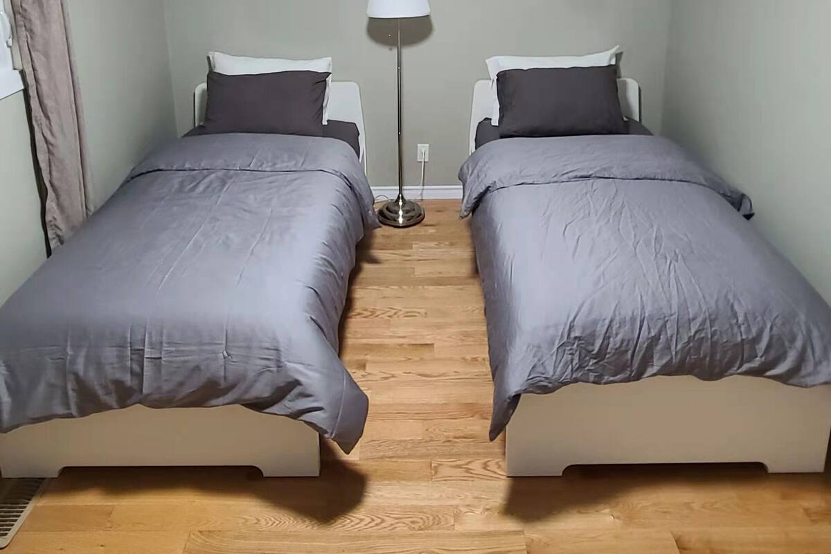 Huoneessa on kaksi sänkyä, kattovalaisin, lattiavalaisin ja seinällä auringonlaskua kuvaava taulu.