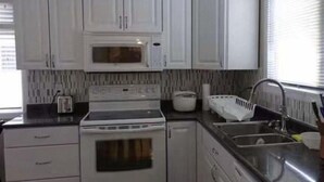 A kitchen with white cabinets, a microwave, a stove, a sink, and a window with blinds. -  YK Aurora B&B  (Yellowknife)