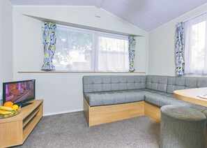 Una sala moderna con un sofá seccional gris, un mueble de televisión de madera con televisor de pantalla plana y una pequeña mesa con una silla.