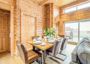A wooden interior with a dining table set for six, leather chairs, and a large window.