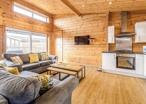 Un intérieur de chalet chaleureux avec un canapé, une table basse, des murs en bois, un téléviseur et un coin cuisine.