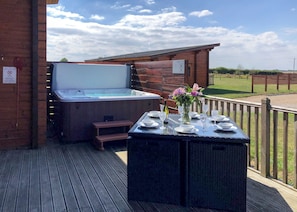 A hot tub on a wooden deck with a table set for dining, surrounded by a wooden fence.