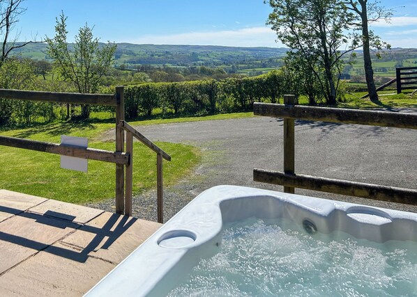 A hot tub with a scenic view of rolling hills and a wooden fence.