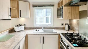 Eine kompakte Küche mit Einbauofen, Mikrowelle, Spüle und Fenster über der Spüle.