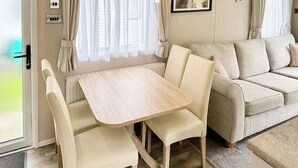 Ein kompaktes Wohnmobil-Interieur mit Esstisch, zwei Stühlen, einer Sitzecke und einem Fenster mit Vorhängen.