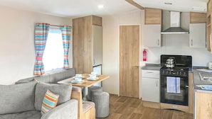 A compact living space with a sofa, a small dining table, a kitchenette, and a door leading to another room. - Caravan with one double and two twin. (Chapel St Leonards, Skegness)