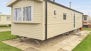 A beige mobile home with a covered porch, a window with curtains, a small door, and a label 'S117'. - Caravan with one double and two twin. (Chapel St Leonards, Skegness)