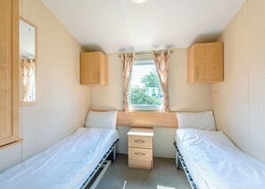 Ein kompaktes Schlafzimmer in einem Wohnmobil mit zwei Betten, einem kleinen Schreibtisch und einem Fenster mit Vorhängen.