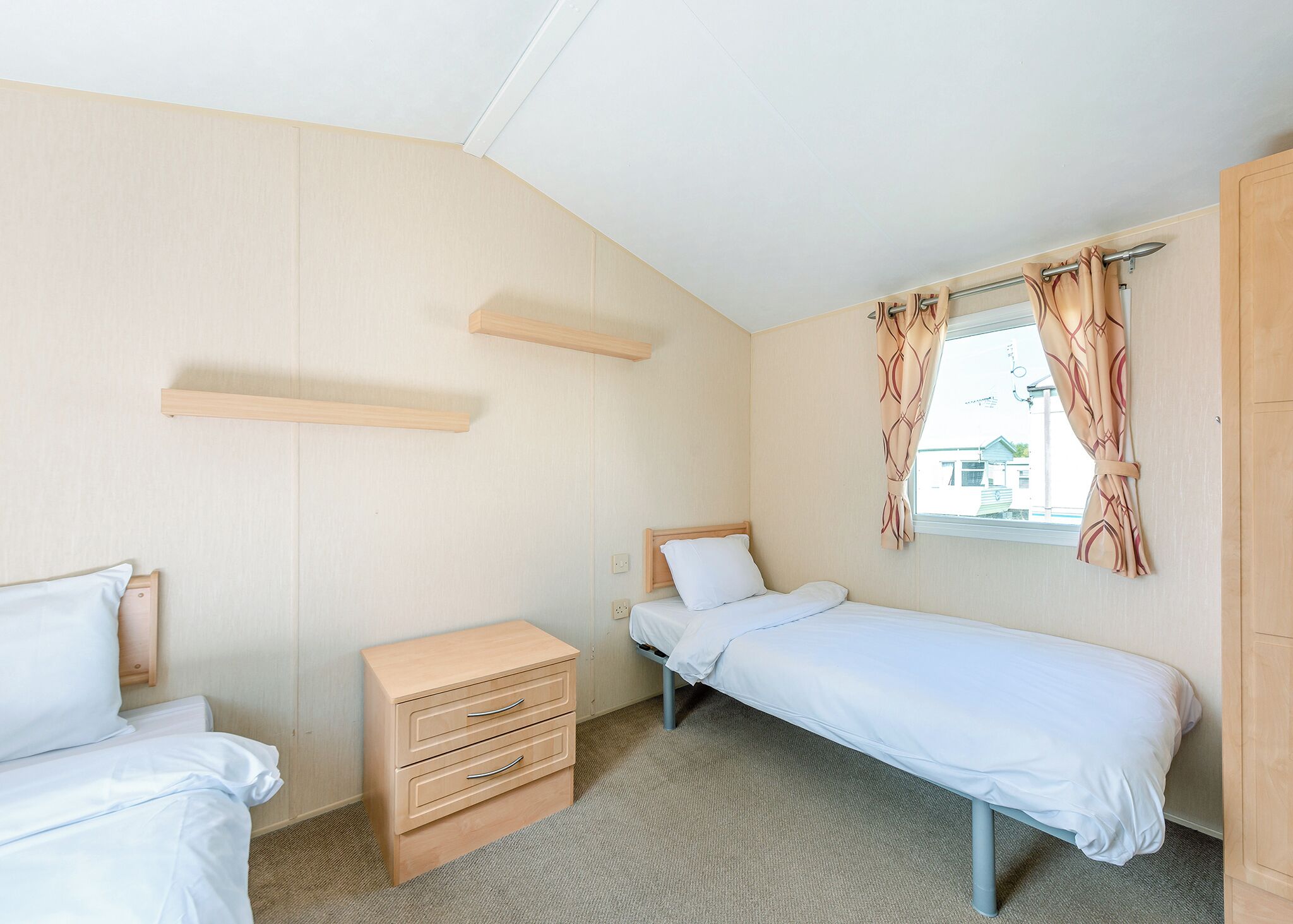 Ein kleines Hotelzimmer mit einem Bett, einem Schminktisch, einem Fenster mit Vorhängen und einem Holzboden.