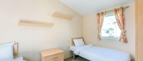 Ein kleines Hotelzimmer mit einem Bett, einem Schminktisch, einem Fenster mit Vorhängen und einem Holzboden.