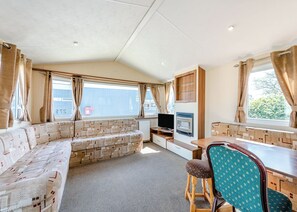 Ein kompaktes Wohnmobil-Interieur mit einer Sitzecke, einem kleinen Tisch, einem Fernseher und einem Fenster mit Vorhängen.