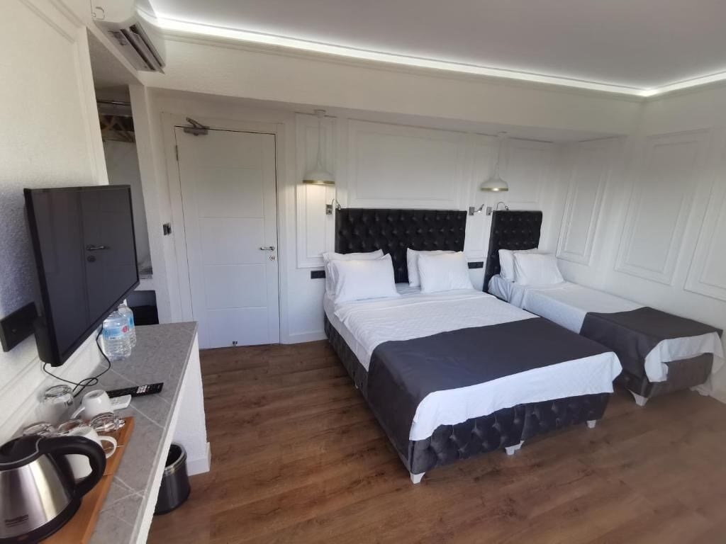 A hotel room with two beds, a TV, a desk with a kettle, and a small table.