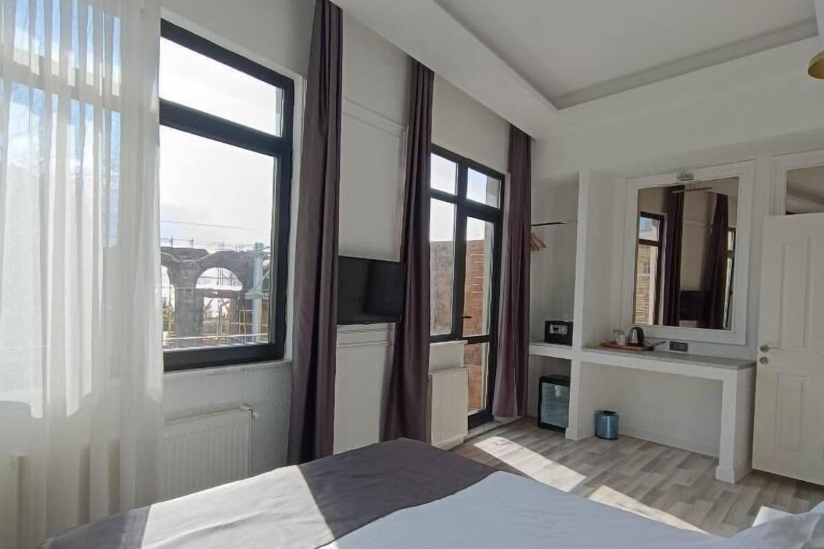 A bedroom with a large bed, a dresser, a mirror, and a window with curtains.