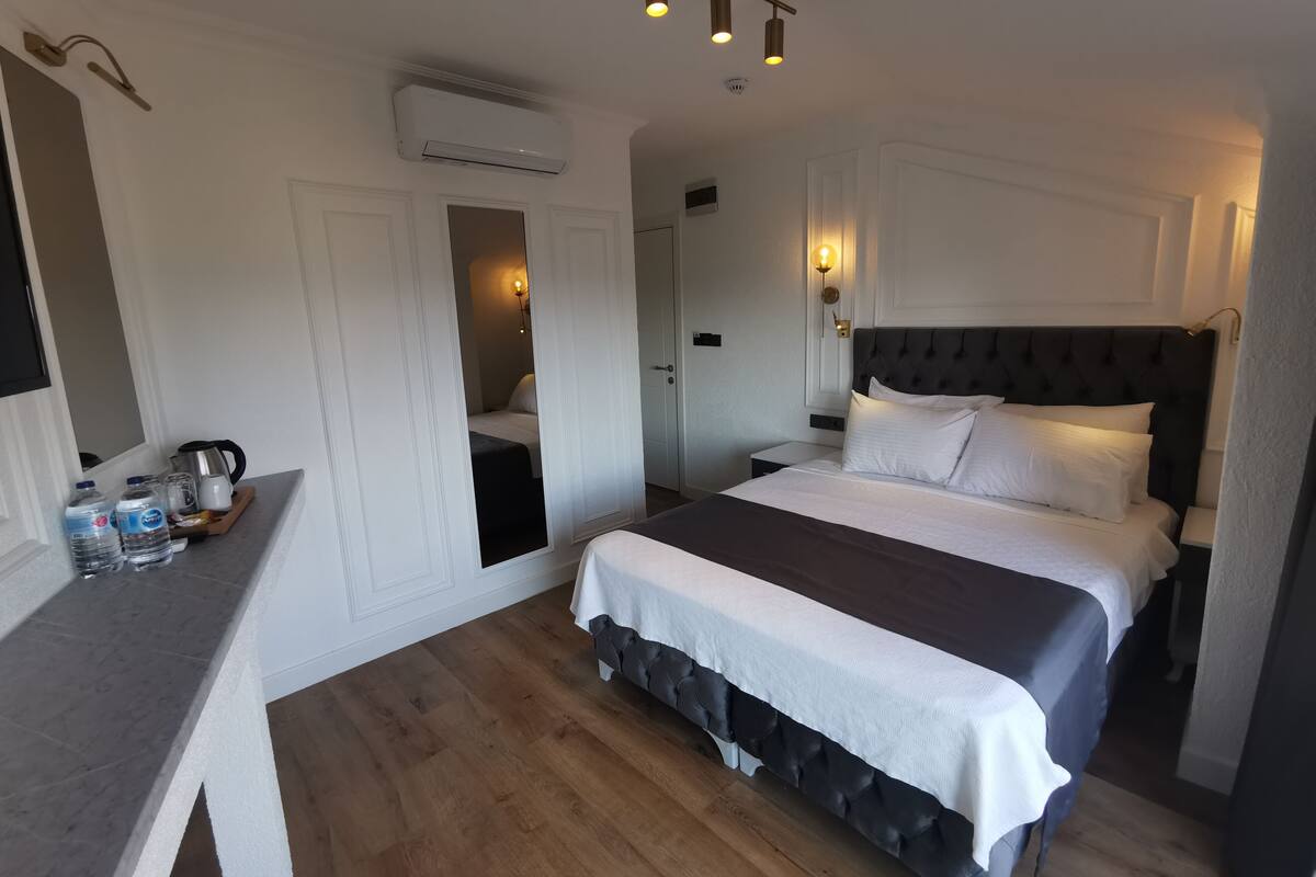 A hotel room with a large bed, a bedside table with a kettle, and a mirror.