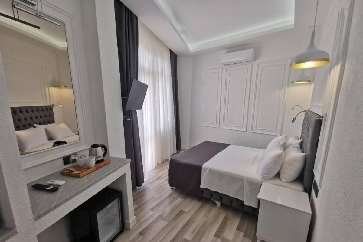 A modern hotel room with a bed, a desk with a coffee maker, a TV, and a wardrobe.