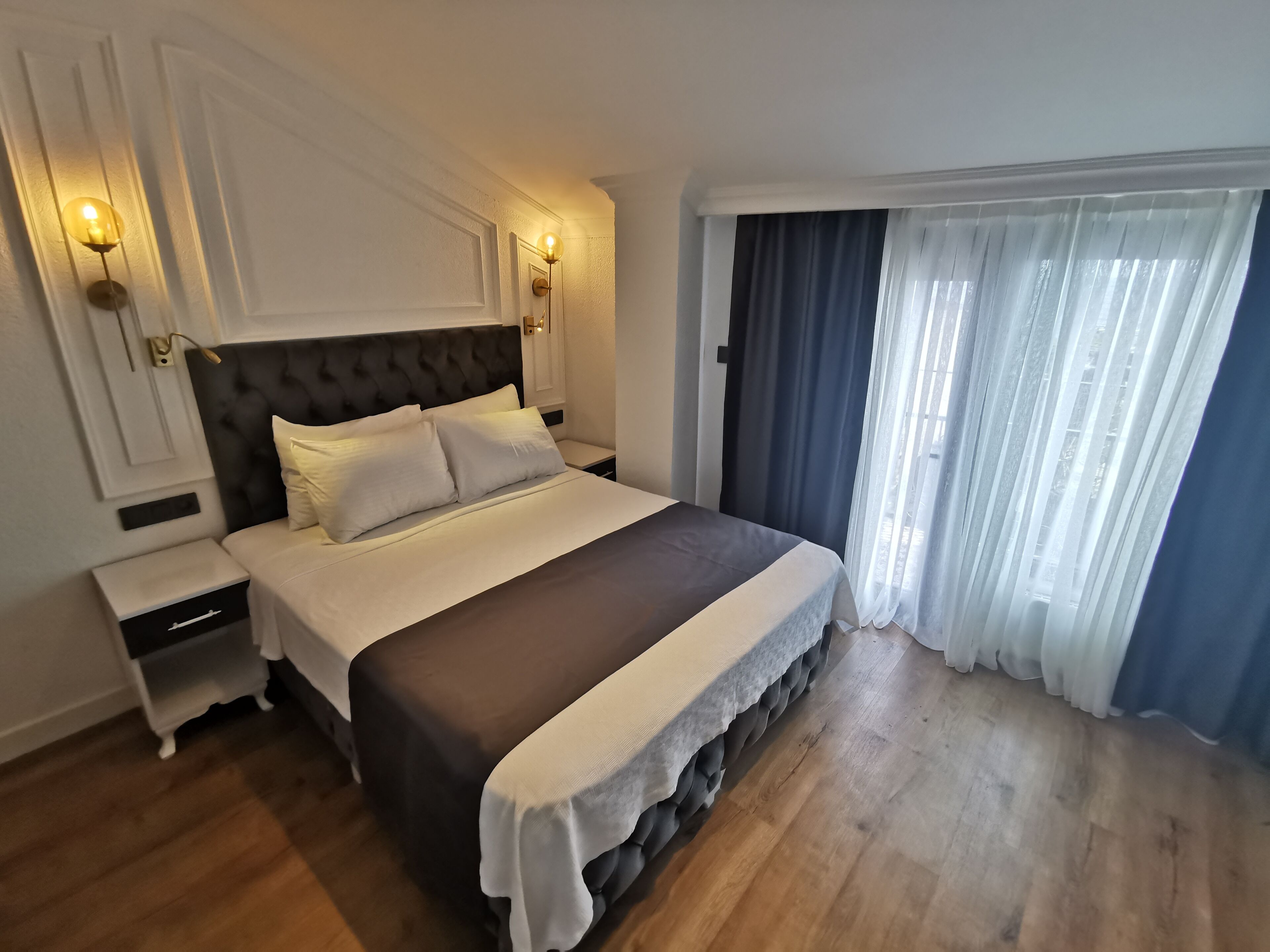 A modern bedroom with a large bed, two bedside tables, and a window with curtains.